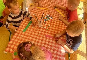 dzieci przy stolikach ozdabiają kolorowymi wydzierankami przepaskę na głowę
