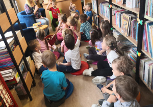 dzieci z zainteresowaniem oglądają zbiory biblioteki i uważnie słuchają pani bibliotekarki