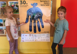 Dwie dziewczynki wskazują na plakat związany z Akcją Sprzątania Świata.