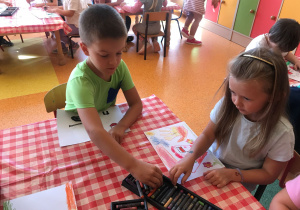 Dzieci siedzą przy stolikach i malują pastelami rysunki na temat Przedszkolaki dla Powstańców.