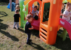 Dzieci bawią się na urządzeniach w ogrodzie przedszkolnym.