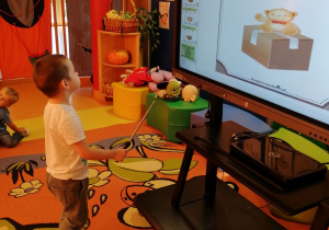 Chłopiec będzie wskazywał gdzie na monitorze interaktywnym jest miś.