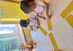 Dzieci siedzą przy stoliku i wykonują świeczkę z wosku pszczelego.
