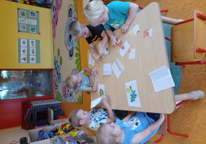 Dzieci siedzą przy stoliku i układają części z obrazka w całość.