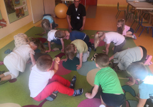 Dzieci wspólnie z panem fizjoterapeutą wykonują ćwiczenia na dywanie.