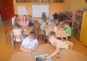 Przedszkolaki siedzą przy stolikach i ozdabiają naklejki wodoodporne.