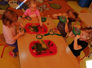 Czwórka dzieci siedzi pry stoliku, na stoliku znajdują się dwie tacki z darami jesieni,