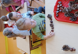 Dzieci siedzą przy stolikach, dzieci układają rytmy z darów jesieni.