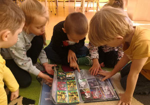Przedszkolaki oglądają klaser z kartami piłkarzy.