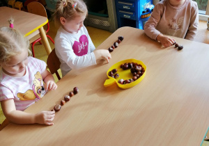 Dzieci siedzą przy stoliku i układają rytm z materiału przyrodniczego.