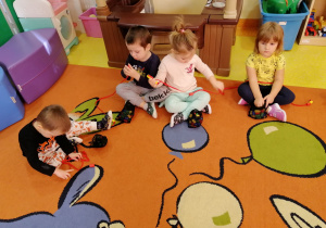 Dzieci siedzą na dywanie i nawlekają klocki numicon na sznurki według właściwej kolejności.