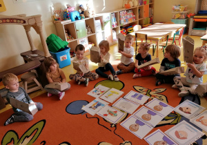 Dzieci siedzą na dywanie, trzymają w rękach papierowe torby, na których nrysowane są różne emocje.