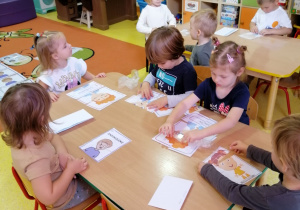 Przedszkolaki siedzą przy stolikach i układają obrazki z części.