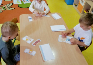 Przedszkolaki siedzą przy stolikach i układają obrazki z części.