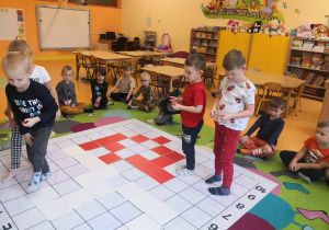 Dzieci siedzą na dywanie, trzech chłopców i jedna dziewczynka odkodowują miejsca tabliczek na macie do kodowania.