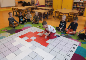 Dzieci siedzą na dywanie, chłopiec odkodowuje miejsce tabliczki na macie do kodowania.