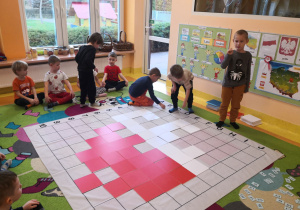 Dzieci siedzą na dywanie, czterech chłopców odkodowuje miejsca tabliczek na macie do kodowania.