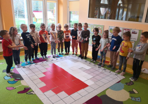 Dzieci stoją wokół maty do kodowania, na której odkodowały kontury mapy Polski.
