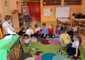 Przedszkolaki siedzą na dywanie, oglądają maskotkę Krasnala Hałabały.
