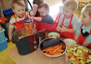 Dzieci wkładają marchewki do sokowirówki.