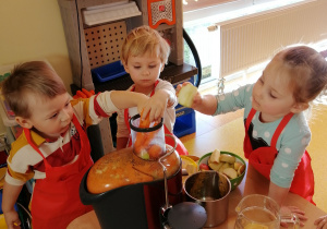 Dzieci wkładają marchewki i jabłka do sokowirówki.
