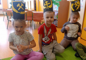 Dzieci pozują do zdjęcia z wykonanymi przez siebie czapkami górniczymi, które mają założone na głowie.