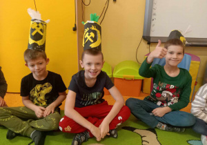Dzieci pozują do zdjęcia z wykonanymi przez siebie czapkami górniczymi, które mają założone na głowie.