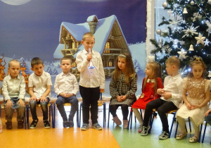 Dzieci siedzą, chłopiec stoi trzyma mikrofon i mówi wiersz.