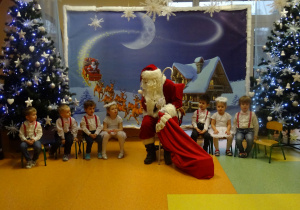 Dzieci siedzą, między nimi siedzi Mikołaj.