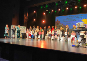 Dzieci stoją z opiekunami na scenie z nagrodami.