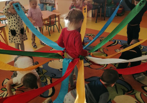 Dziewczynka stoi w środku wiatraka, a dzieci poruszają skrzydłami wiatraka.