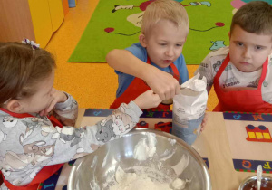 Dziewczynka i chłopiec wsypują do miski mąkę.
