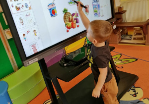 Chłopiec wskazuje na ekranie multimedialnym niezdrowe jedzenie.