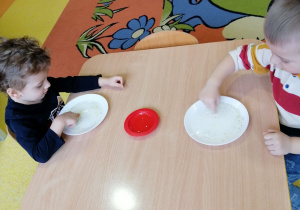 Dzieci siedzą przy stolikach i wykonują zabawę badawczą.