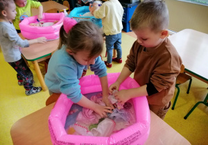 Dzieci kąpią lalki w małych basenach.