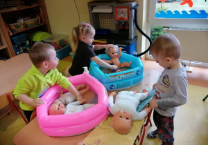 Dzieci kąpią lalki w małych basenach.