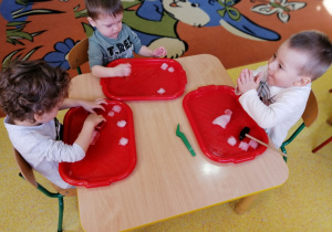 Dzieci siedzą przy stolikach i próbują rozbijać lód.