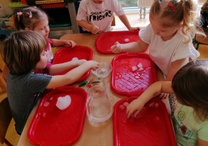 Dzieci siedzą przy stolikach i dotykają lód.