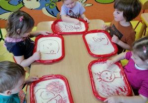 Dzieci rysują palcem w mące.