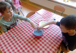 Dzieci dotykają patyczkami z detergentem mleka.