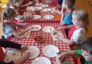 Dzieci siedzą przy stolikach i wykonują wielkanocne zajączki z warzyw i jajek.