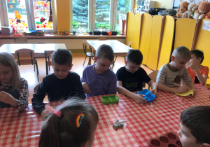 Dzieci siedzą przy stolikach i wykonują mydełka.