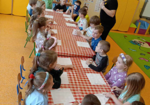 Dzieci siedzą przy stolikach i słuchają Pani Pauliny.