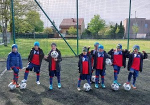 Chłopcy stoją w strojach piłkarskich z piłkami.