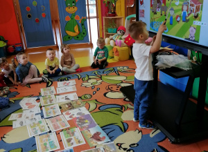 Dzieci siedzą na dywanie, chłopiec wskazuje zwierzęta na tablicy interaktywnej.