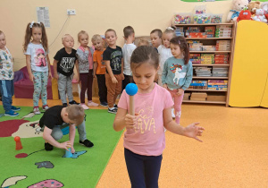 Dziewczynka idzie z piłką na drewnianej postawce, uważa, żeby piłka nie spadła.