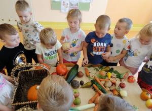 Dzieci stoją przy stoliku, na stoliku leżą warzywa, dzieci je oglądają, dotykają.