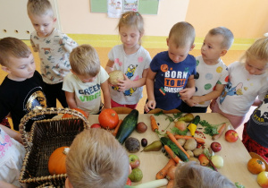 Dzieci stoją przy stoliku, na stoliku leżą warzywa, dzieci je oglądają, dotykają.